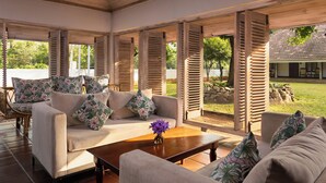 Un espacio al aire libre techado con una mecedora y sillas, contraventanas de madera y vistas a una casa.