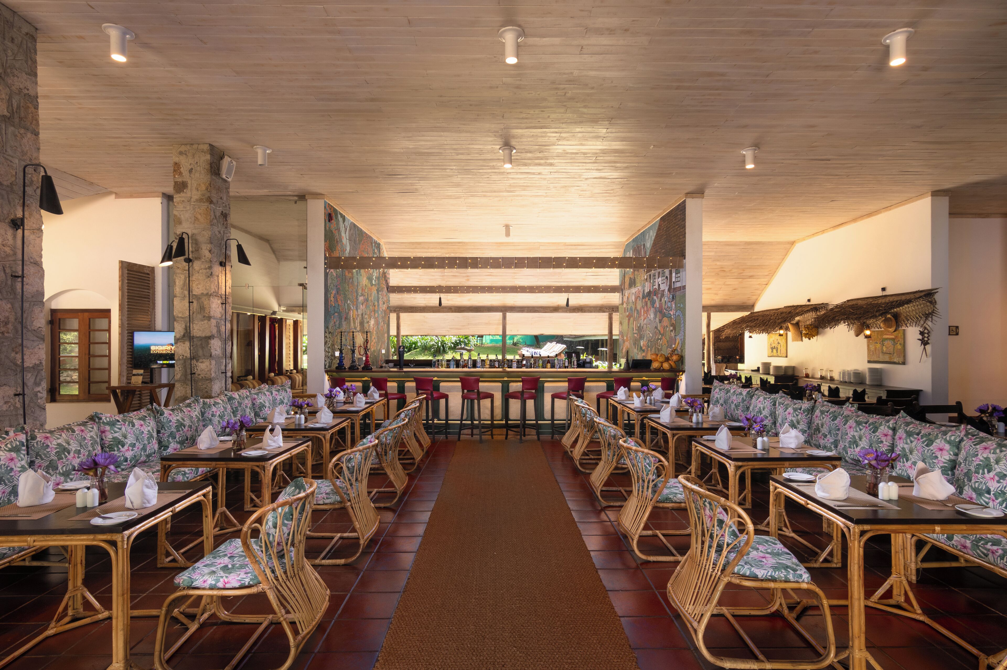 Ein Restaurant mit langen Gemeinschaftstischen und Sitzecken, Holzboden und Blick ins Freie.