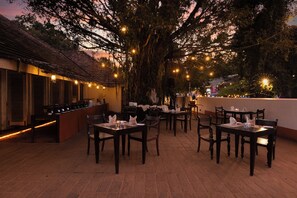An outdoor dining area with tables and chairs, string lights, and a large tree. - EKHO Sigiriya (Sigiriya)