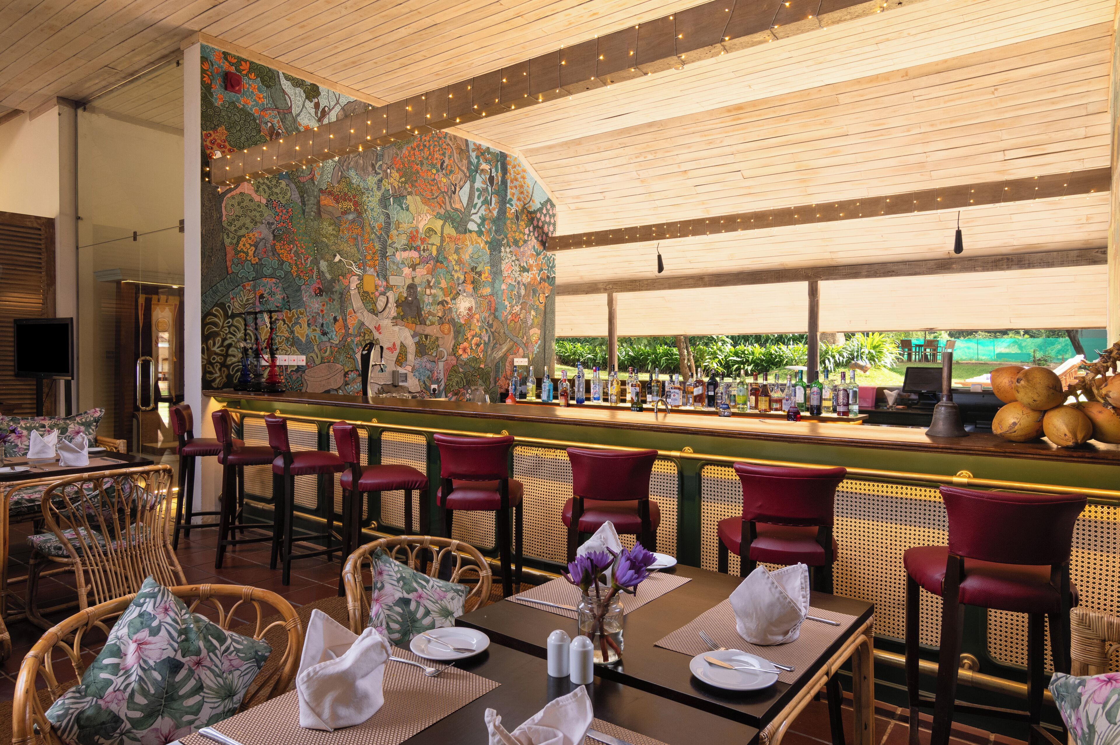 Een restaurant met een bar, rieten stoelen en een muurschildering.