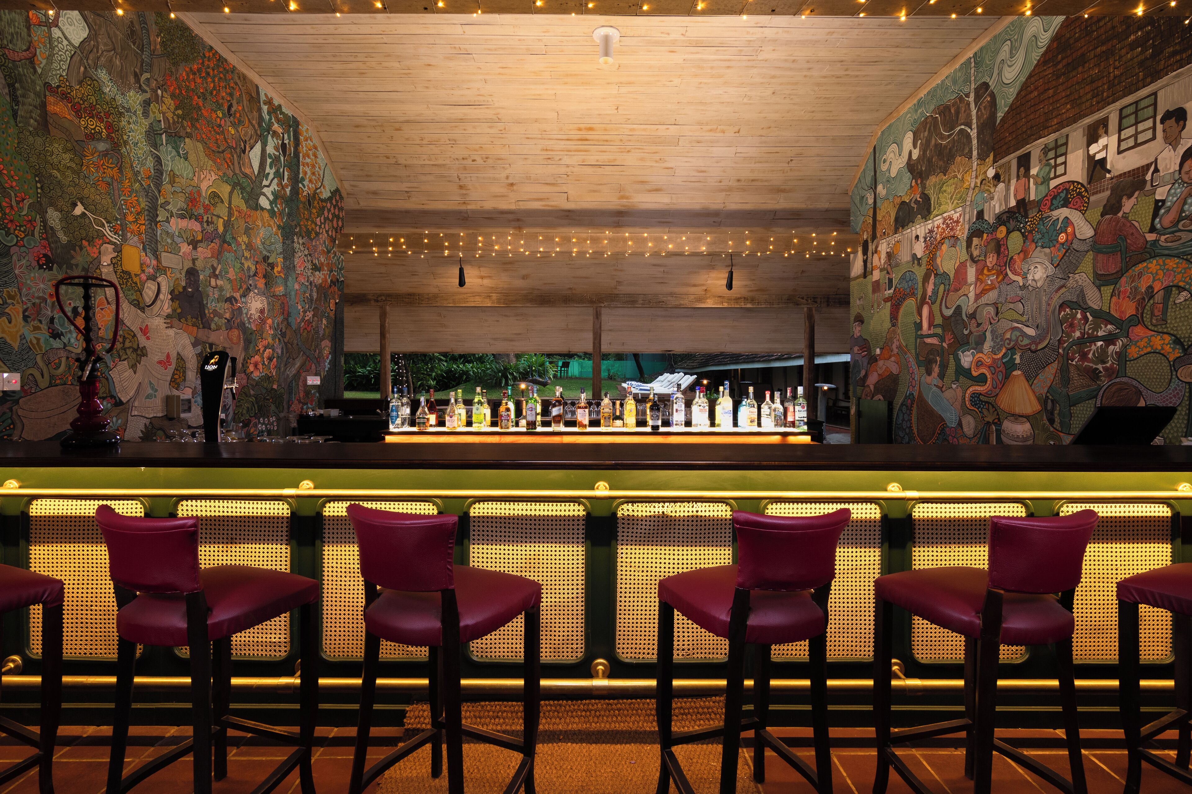 A bar area with a mural, bar stools, and a counter.