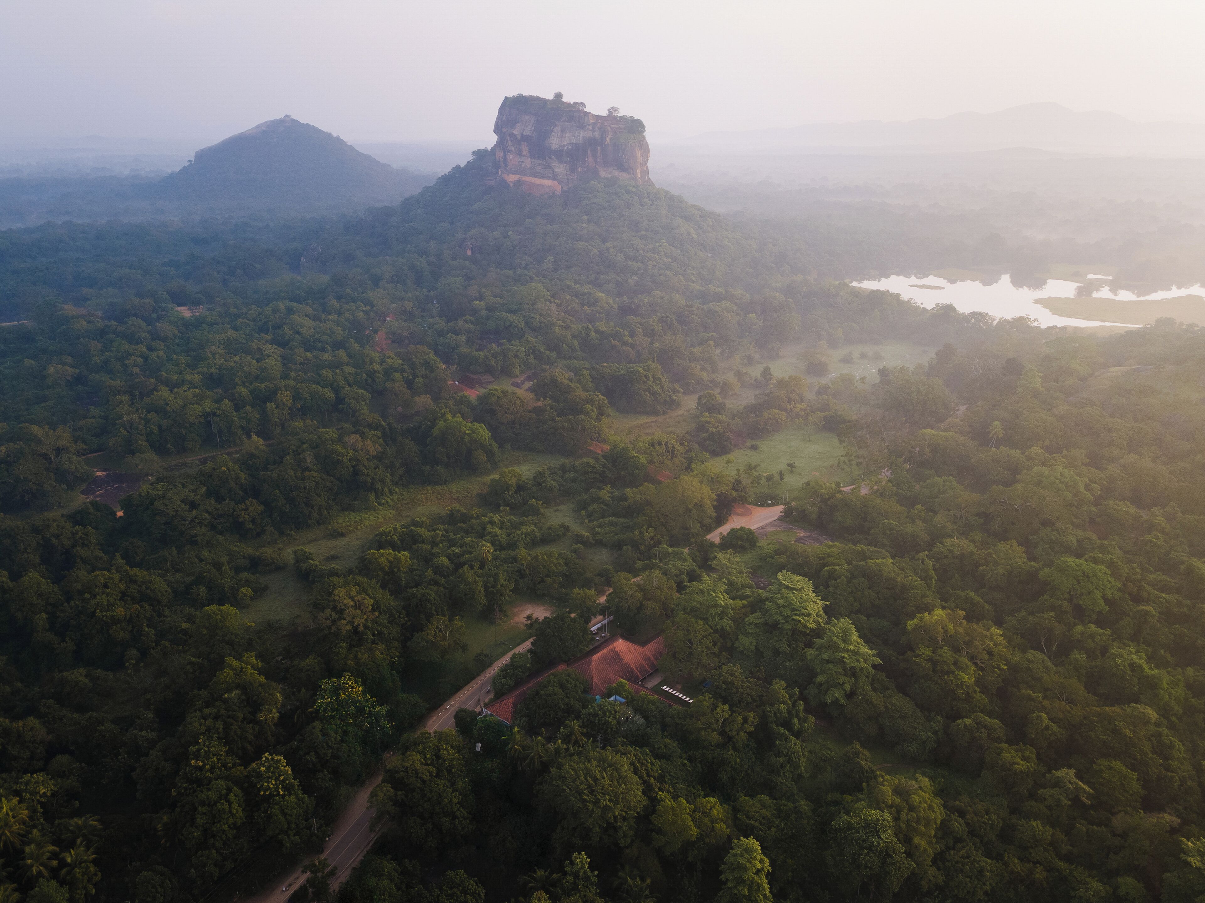 An aerial view of a forested area with a prominent rocky outcrop and a small building with a red roof.