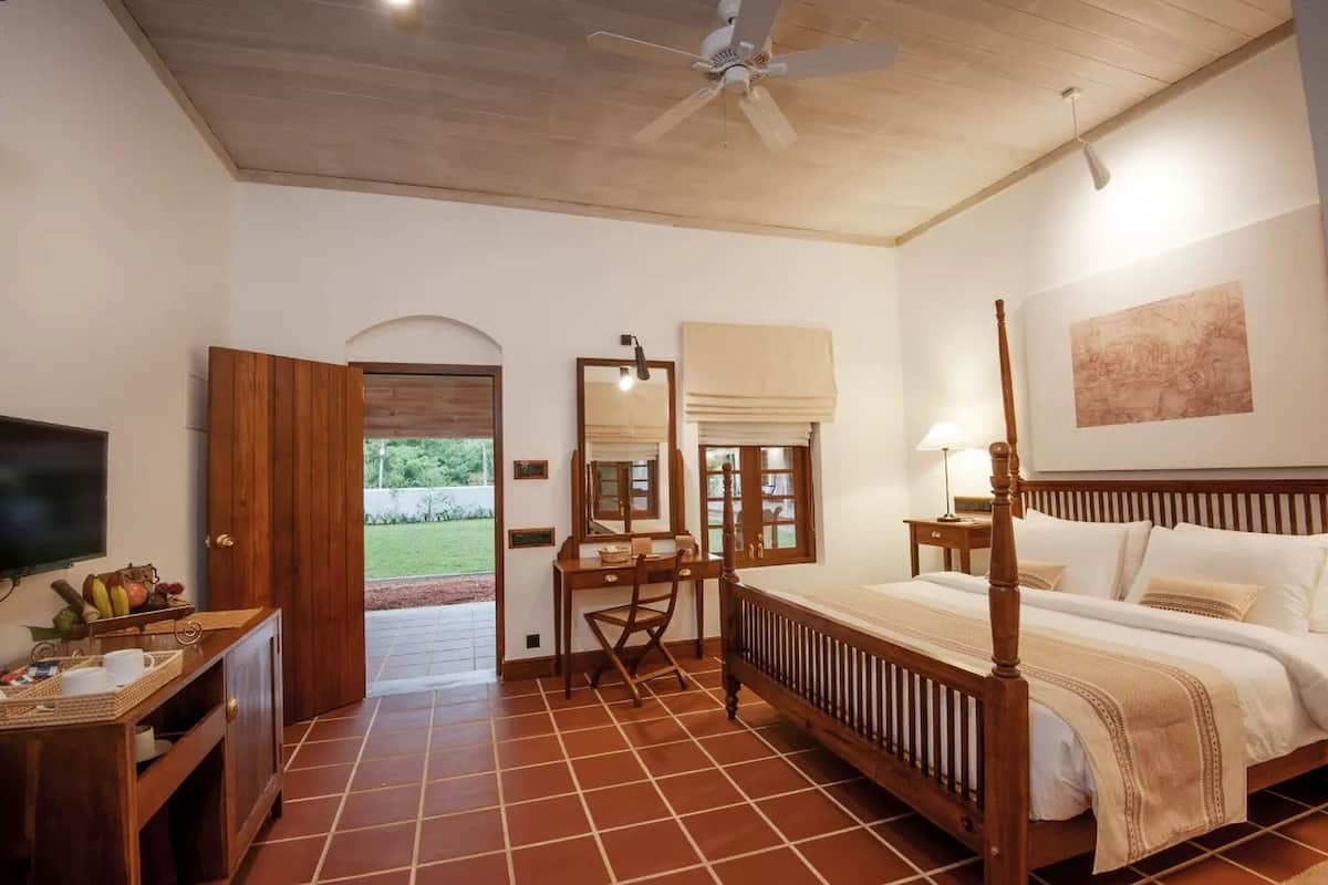 Une chambre à coucher avec un lit à baldaquin, un bureau avec une chaise, une télévision et une vue sur l’extérieur.
