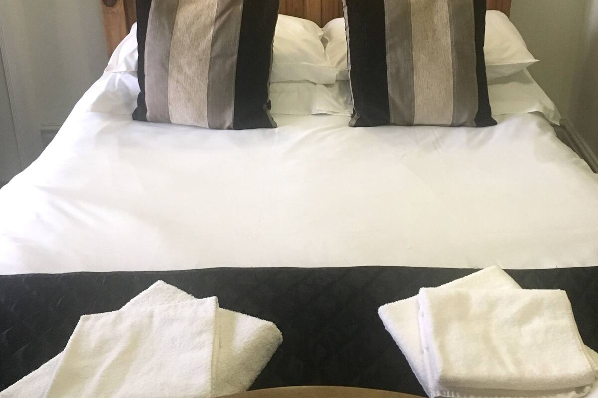 Un lit bien fait, avec une tête de lit en bois, du linge de lit blanc et deux oreillers.