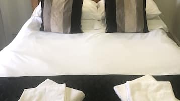 A neatly made bed with a wooden headboard, white linens, and two pillows.