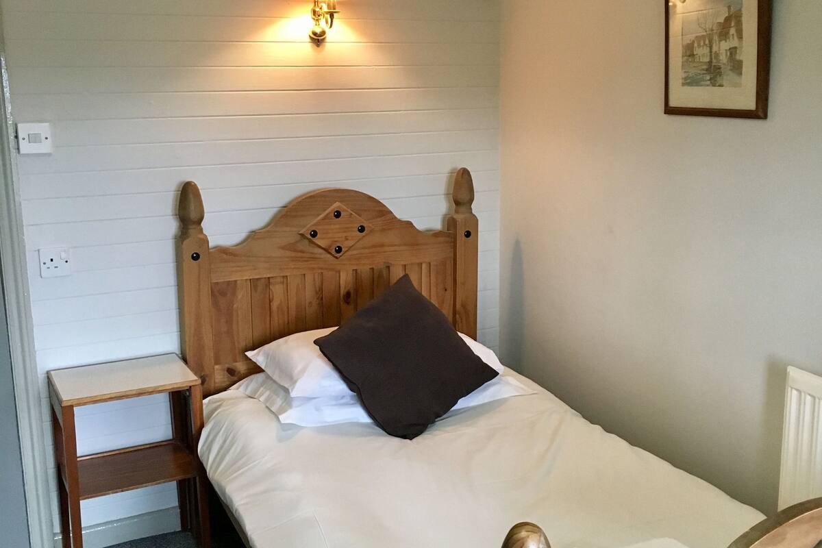Un lit bien fait, avec une tête de lit en bois, une table de chevet et une lampe fixée au mur.