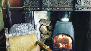 Una chimenea tradicional con intrincados grabados, una silla de madera con cojín y una pared de piedra.