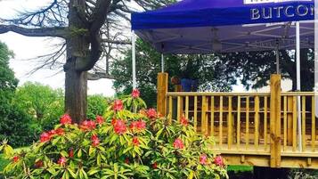 A gazebo with a wooden deck, surrounded by lush greenery and a small pond.
