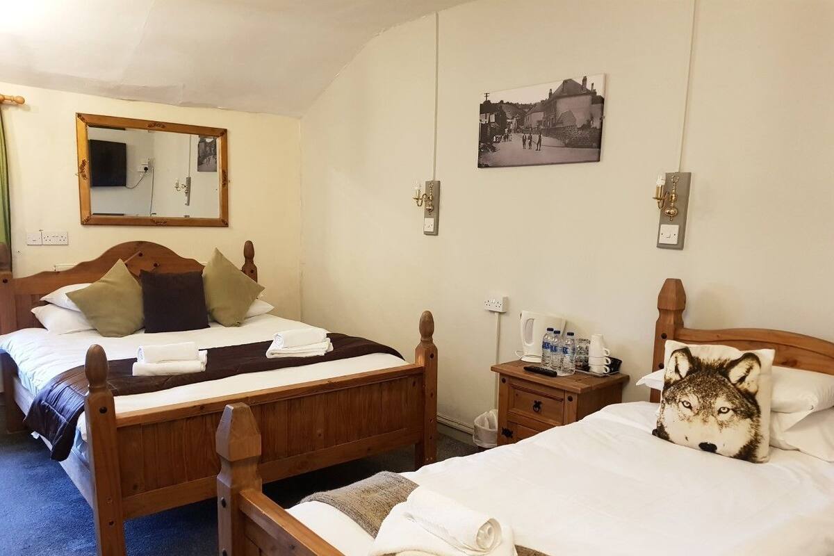 Une chambre d’hôtel avec deux lits en bois, un miroir, un tableau accroché au mur et une table de chevet avec une bouilloire et des bouteilles.