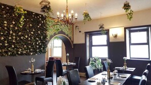 Restaurante con interior oscuro, ventanas amplias y una pared cubierta de vegetación. Las mesas están dispuestas con flores blancas y velas.