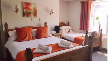 Une chambre d’hôtel avec deux lits en bois, une literie orange, un tableau au mur et une fenêtre avec des rideaux.