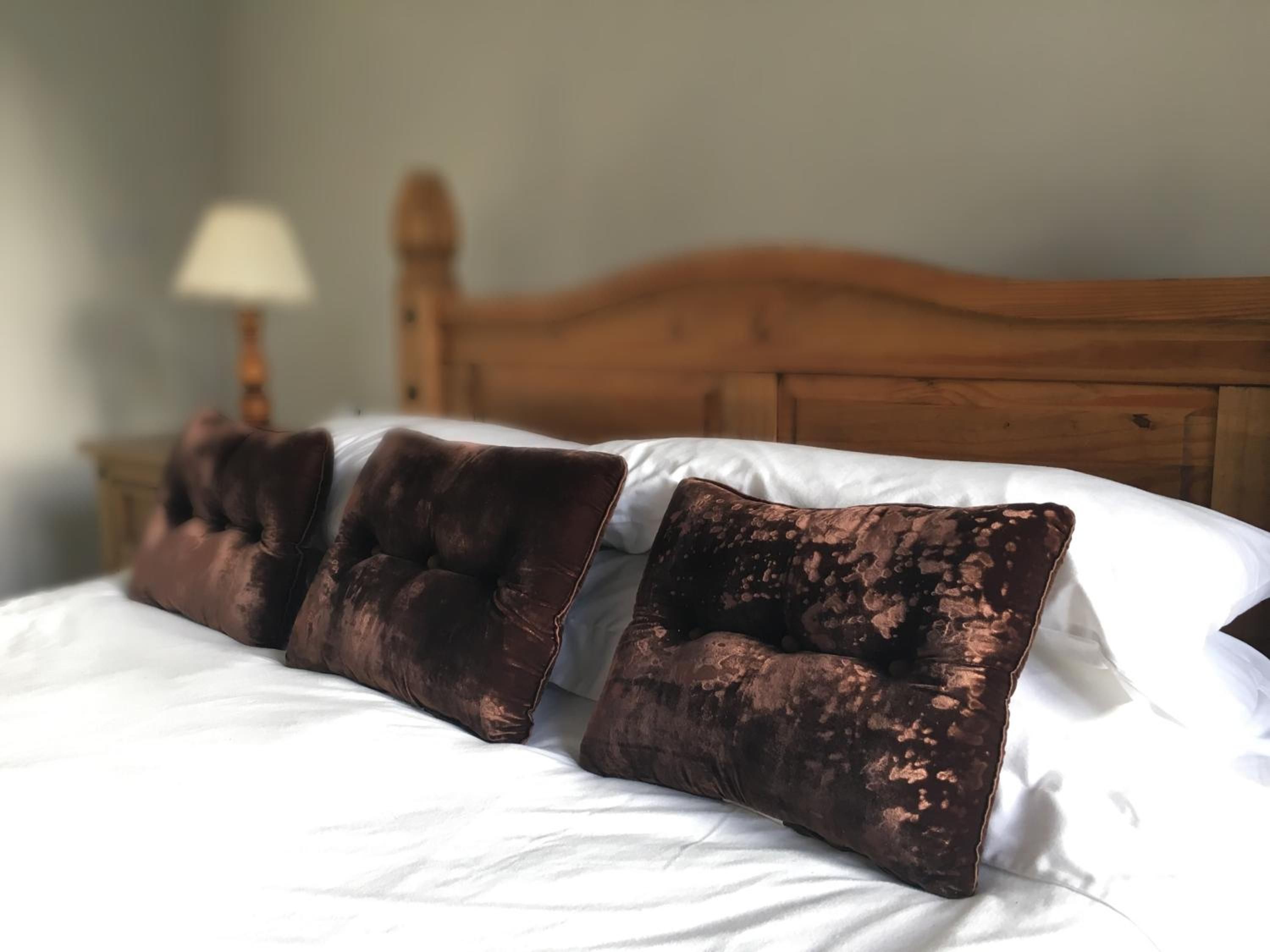 A bed with white linens and three brown pillows.