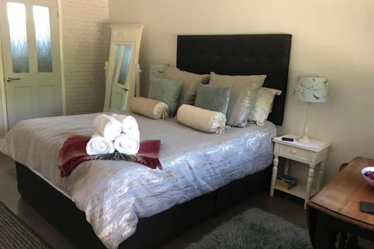 Een opgemaakt bed met opgerolde handdoeken, een hoofdbord en een nachtkastje met een lamp.