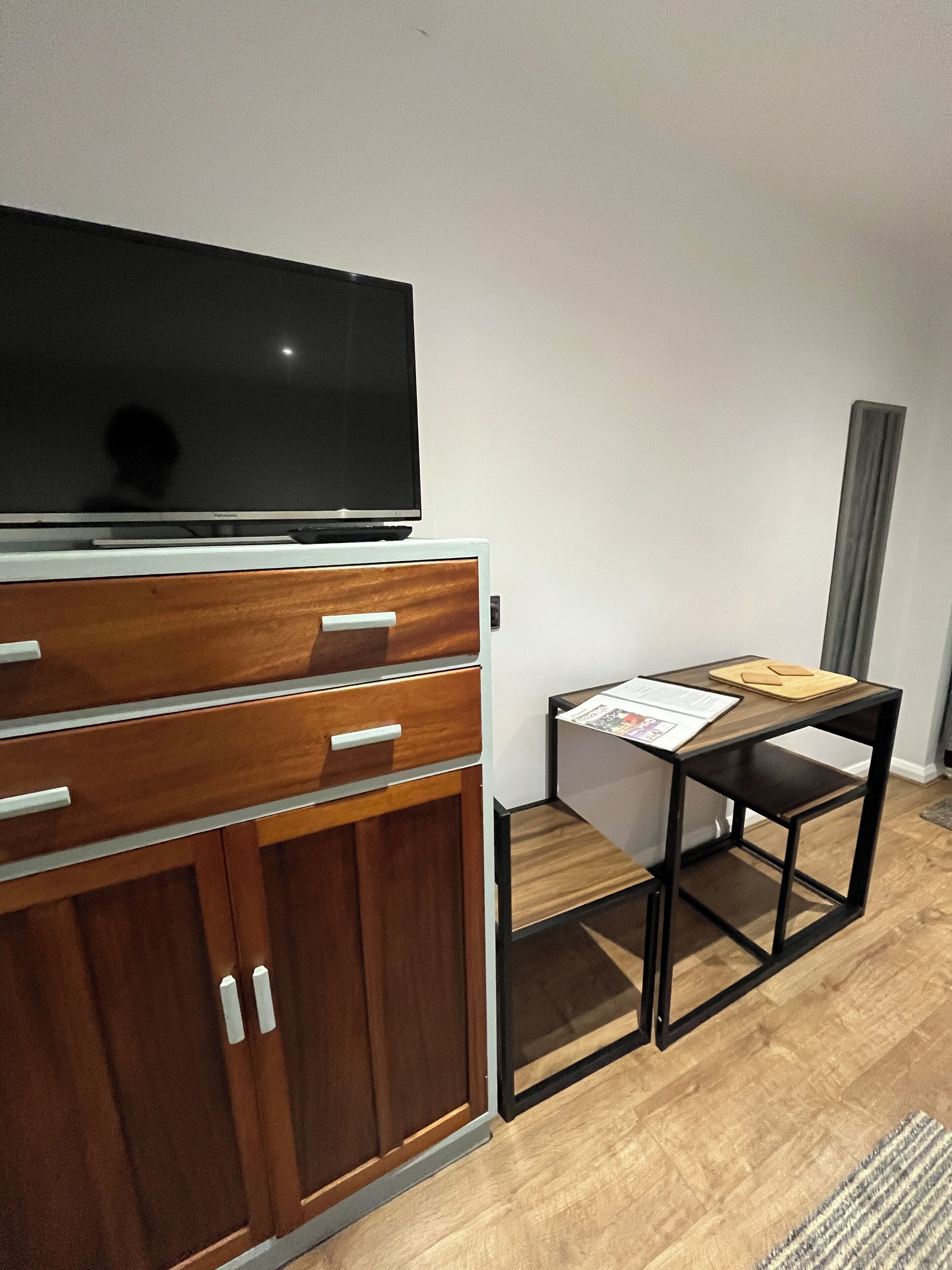 A room with a wooden cabinet, a television on top, a small table with papers, and a grey curtain.