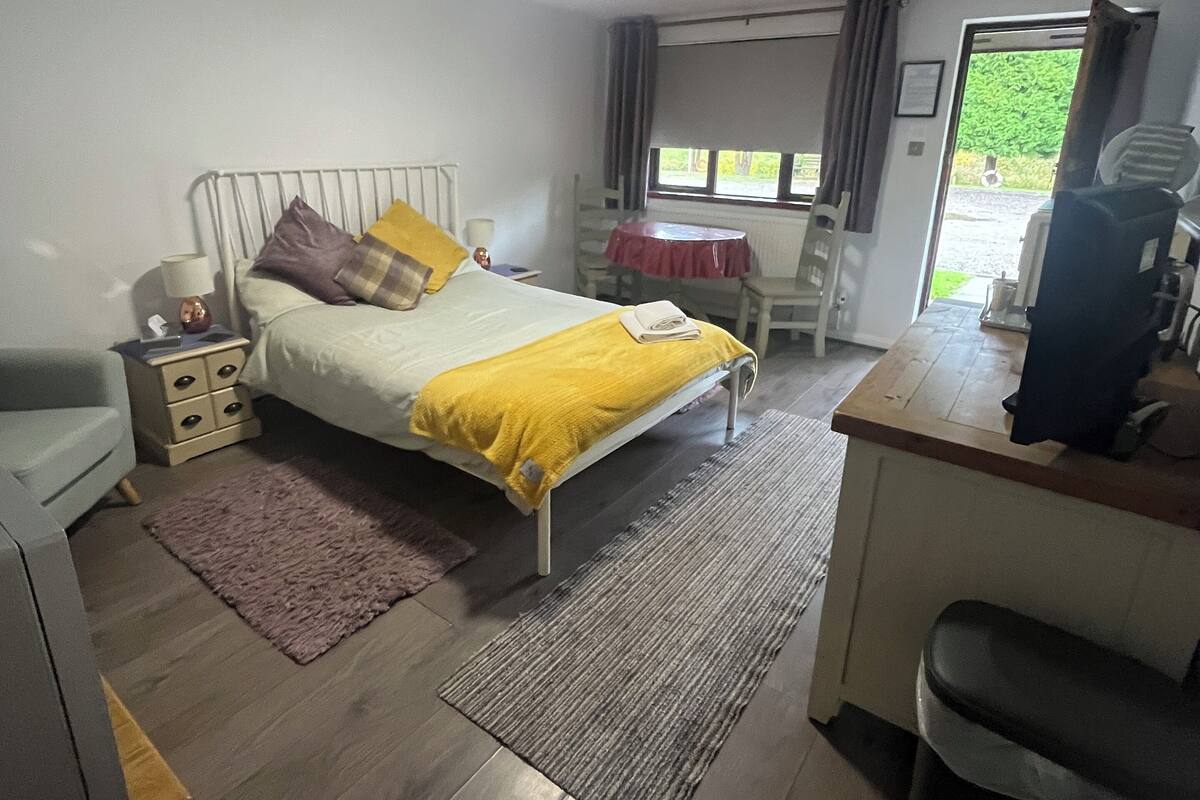 Een slaapkamer met een bed, nachtkastje, lamp, bureau, stoel en uitzicht op het landschap.