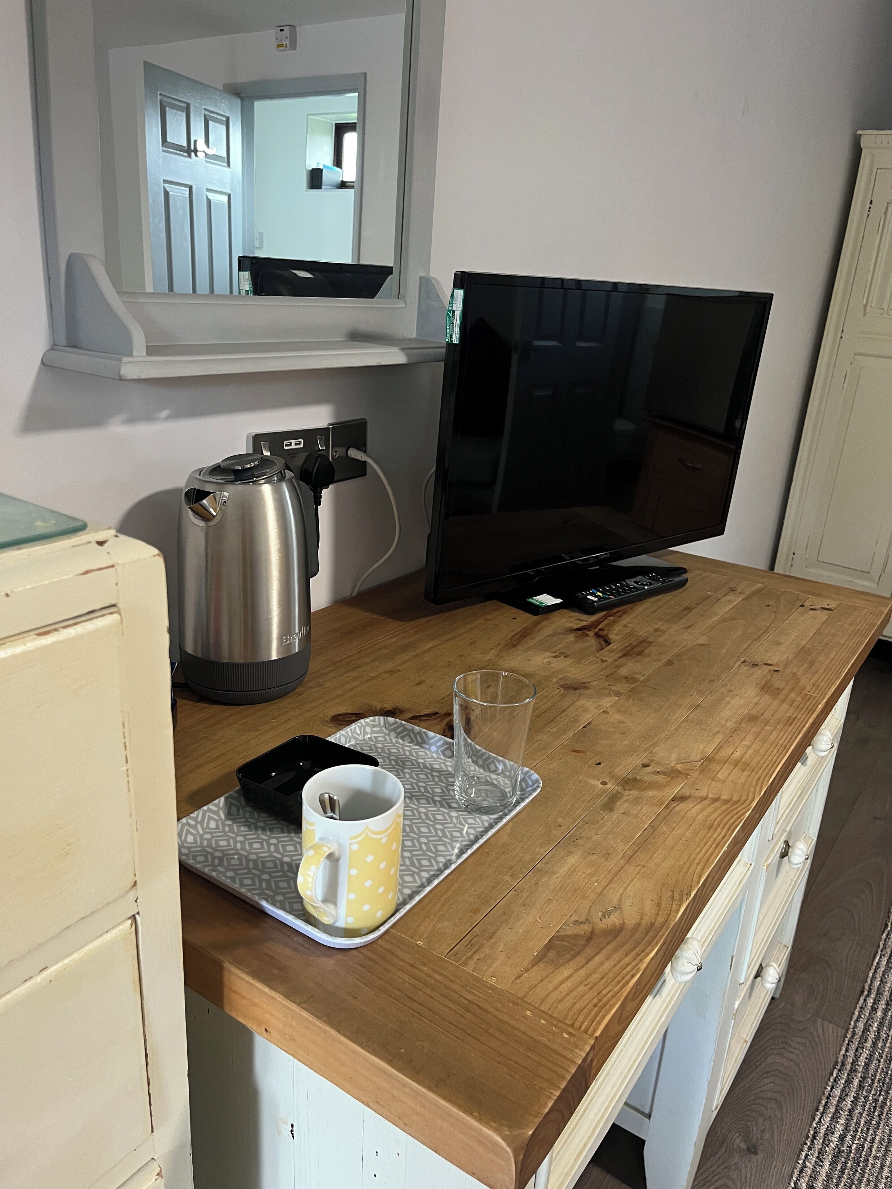 Un comptoir de cuisine en bois avec une machine à café, une tasse et un verre. Une télévision est posée sur le comptoir, et une armoire blanche se trouve à droite.