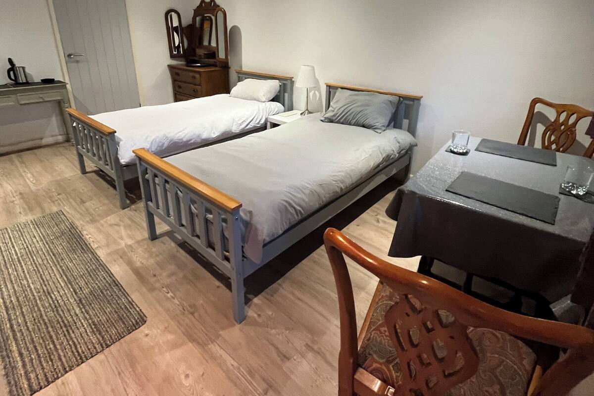 Een slaapkamer met twee eenpersoonsbedden, een houten nachtkastje, een tafel met stoel, een spiegel en een deur.