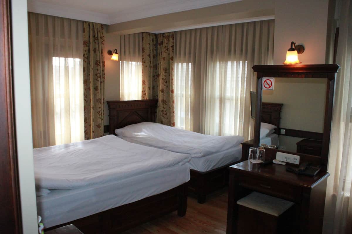 A hotel room with two single beds, a wooden dresser, a desk with a telephone, and a mirror.