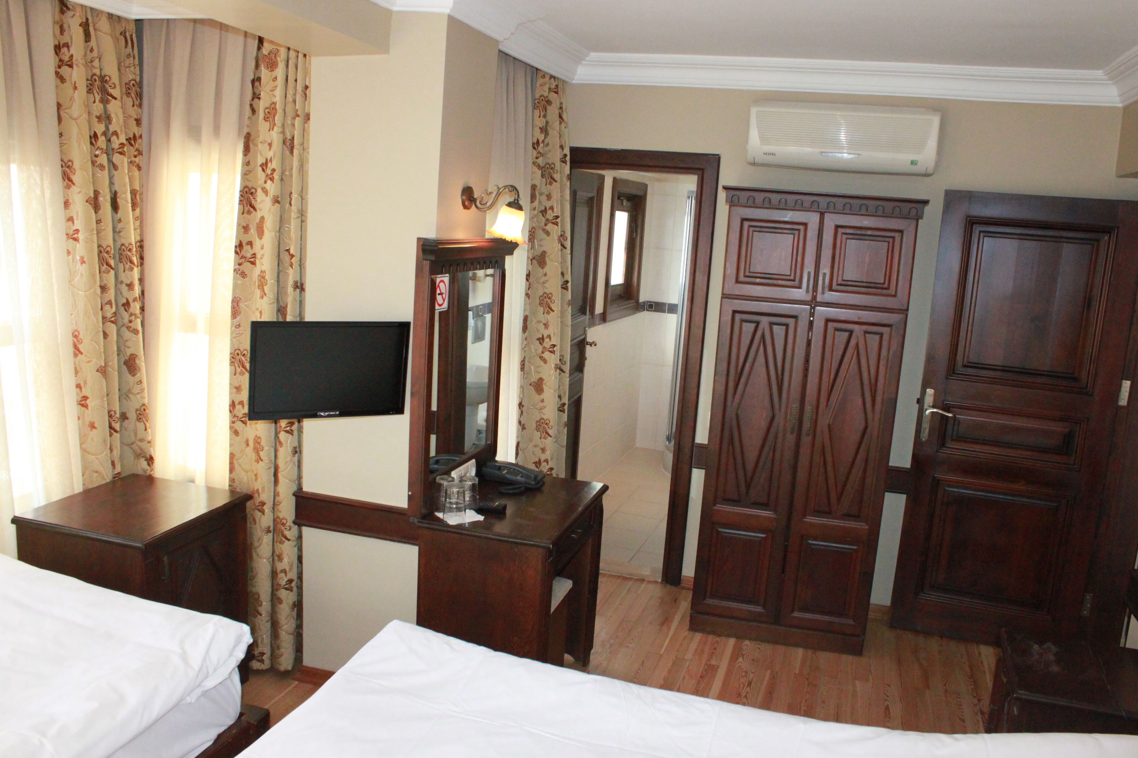 A hotel room with two beds, a desk with a television, a mirror, and wooden wardrobes.