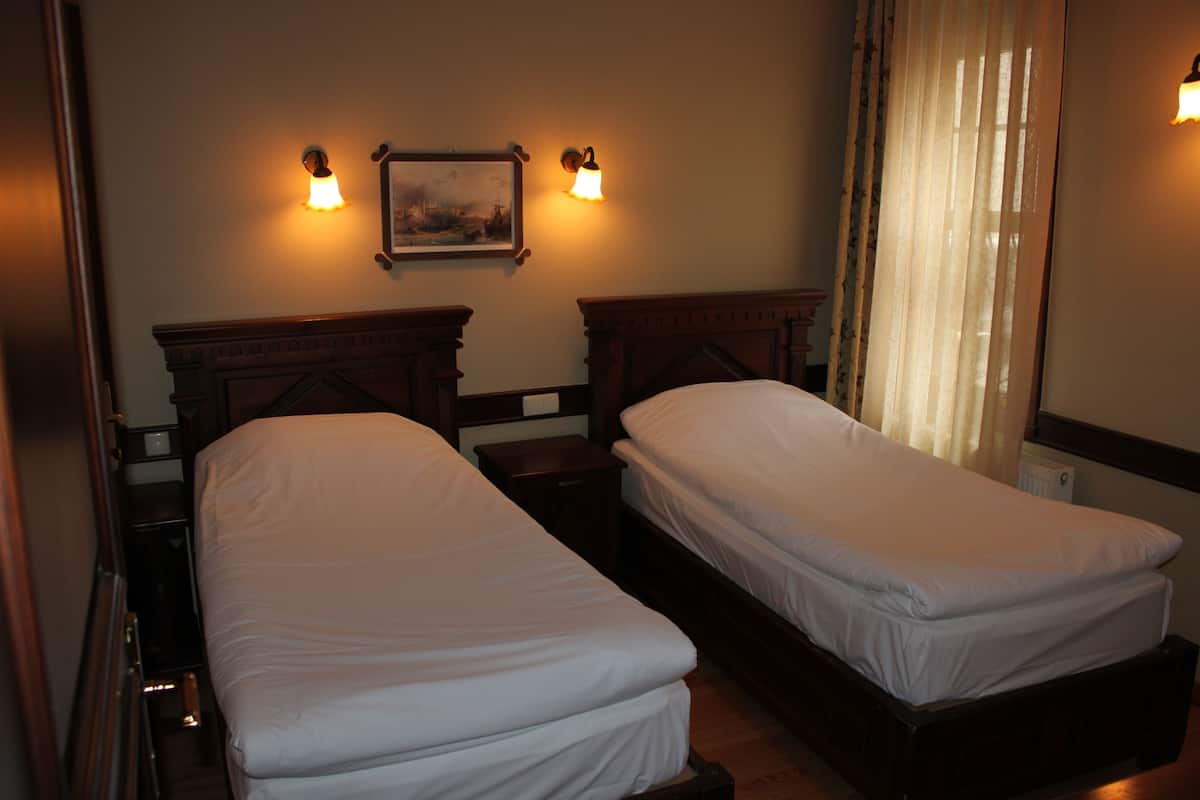 A hotel room with two single beds, a nightstand, a framed picture on the wall, and a window with curtains.