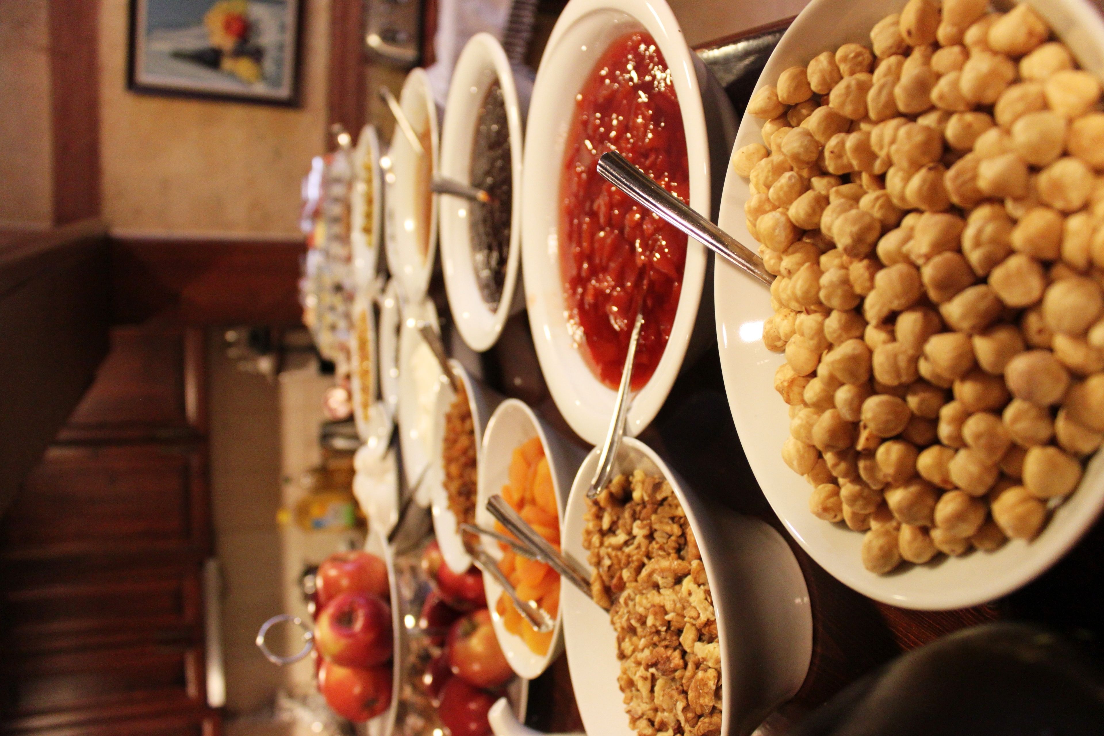 A buffet with various food items including fruits, granola, and a large bowl of chickpeas.