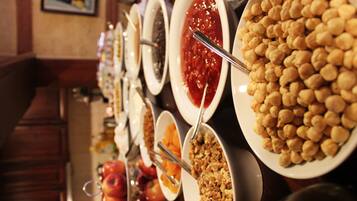 A buffet with various food items including fruits, granola, and a large bowl of chickpeas.