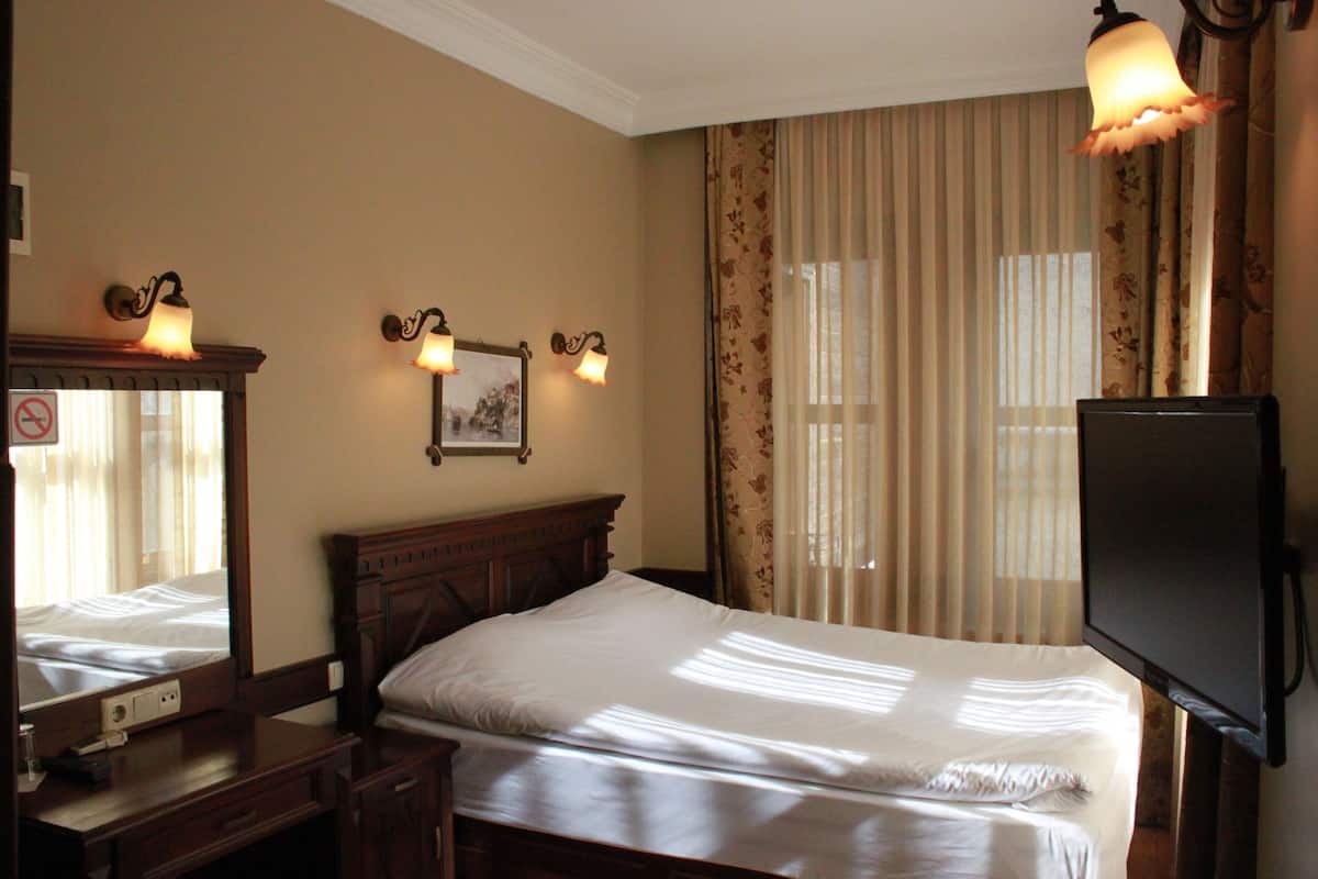 A hotel room with a bed, a desk with a lamp, a television, and a window with curtains.