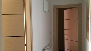 A hallway with a wooden door on the left, a radiator on the wall, and a wooden cabinet with drawers on the right. - NL Smart (Rome)