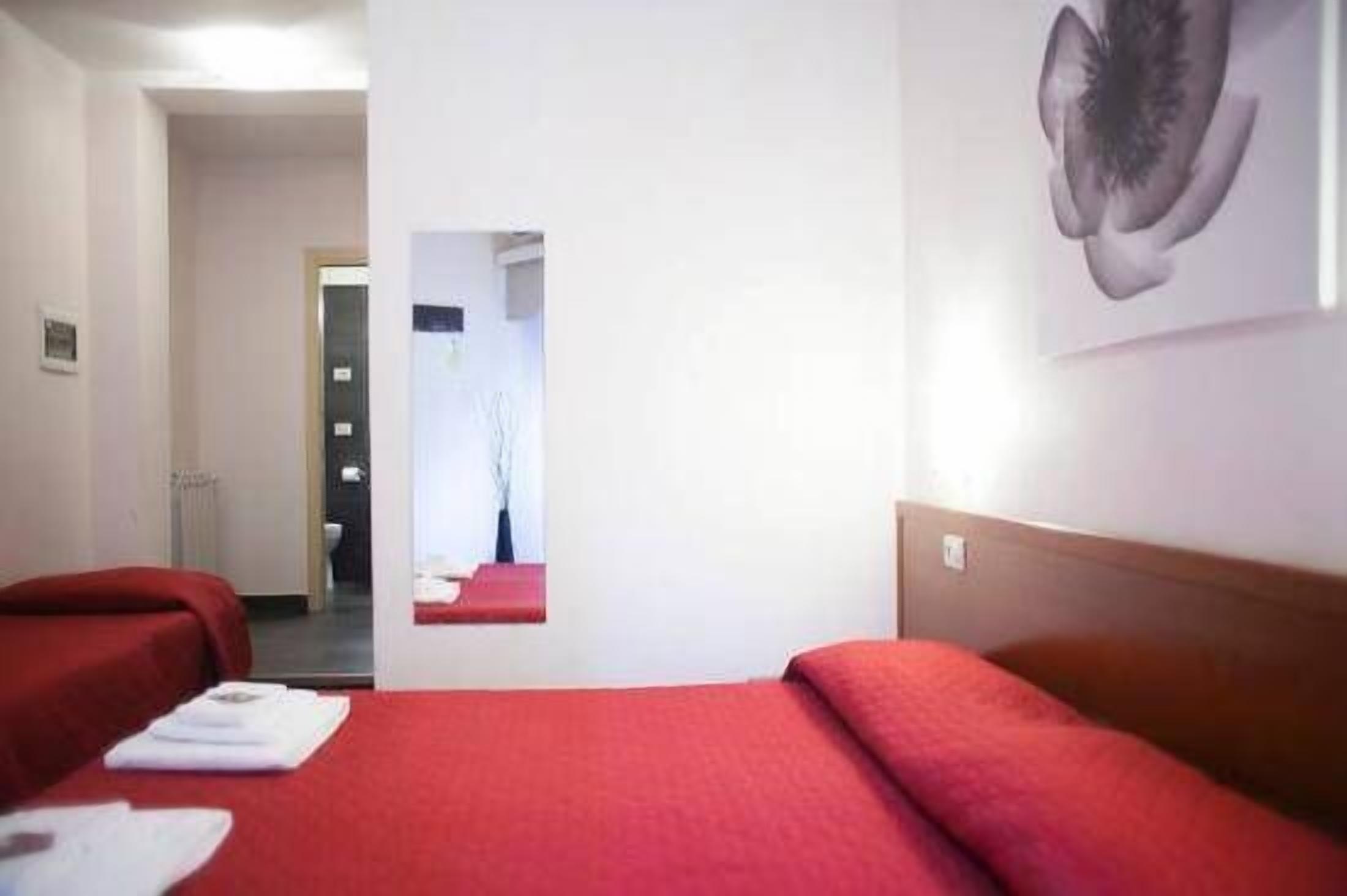 A hotel room with a red bedspread, a mirror, and a wall-mounted artwork.
