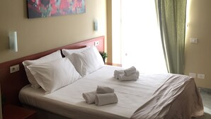 A hotel room with a bed, pillows, a nightstand, a painting on the wall, and a window with curtains. - NL Smart (Rome)