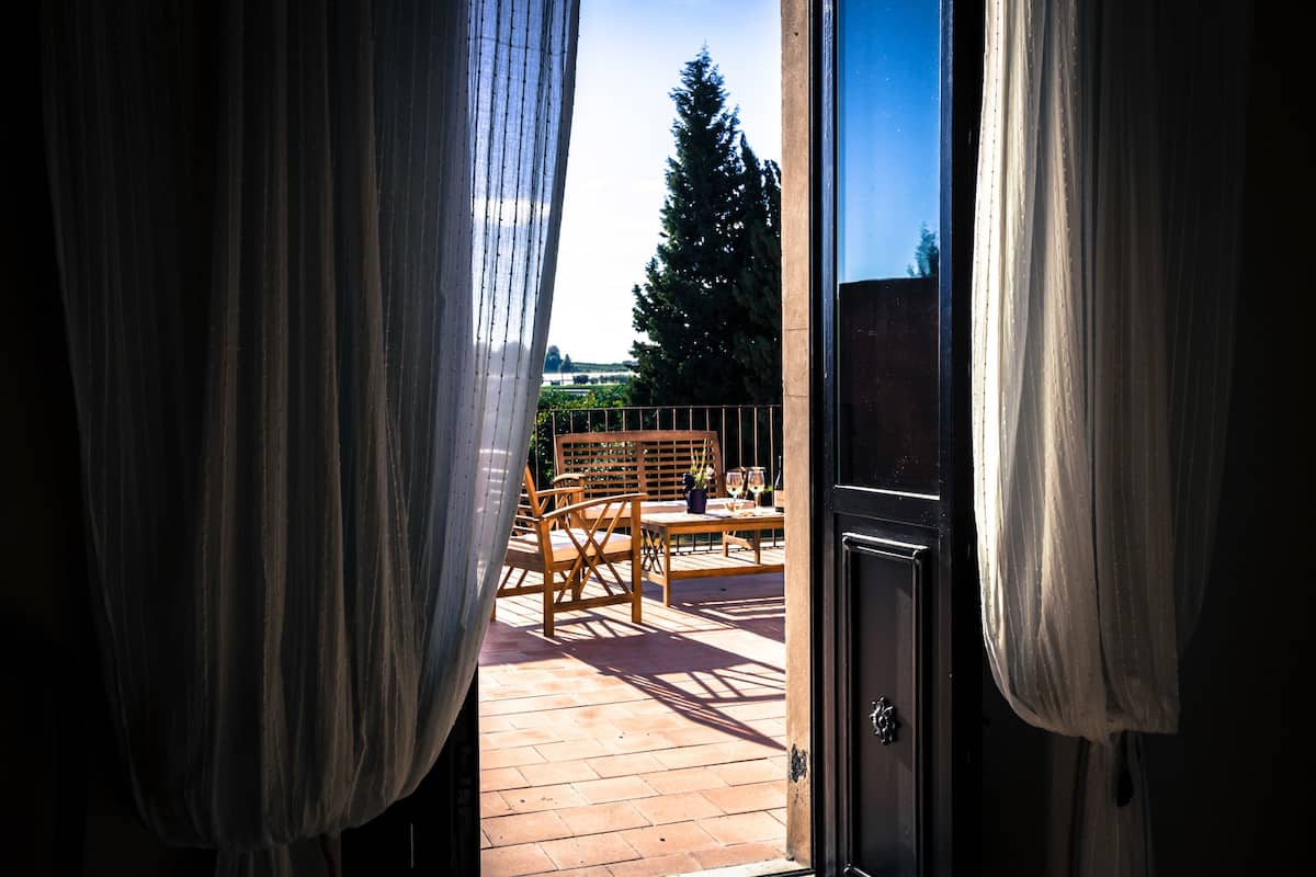 An open door to a balcony with wooden furniture and a view of a tree and sky.