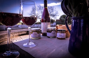 Two wine glasses, a wine bottle, and two jars of olive oil on a wooden table outdoors. - Tenuta del Gelso (Catania)