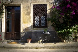 A building with a brown door and window, a small outdoor table with chairs, and potted plants. - Tenuta del Gelso (Catania)