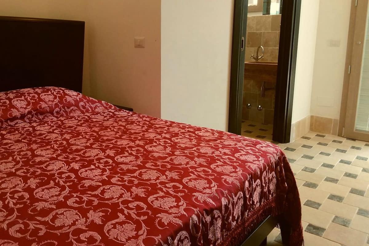 Un dormitorio con cama, un baño con lavabo y espejo, y suelo de baldosas.