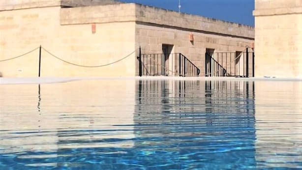 A swimming pool with clear water, surrounded by stone walls and metal railings. - La Trottoria (Otranto)