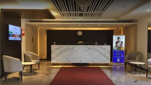 Una zona de recepció d'hotel amb un taulell de marbre, una catifa vermella i cadires modernes.