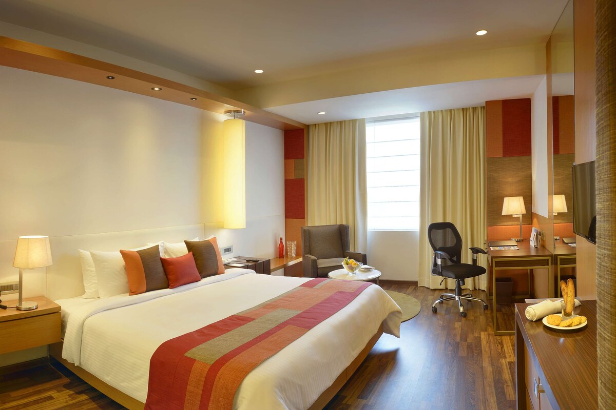 Habitación de hotel con una cama grande, un escritorio con una silla, un televisor y una ventana con cortinas.