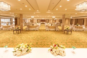 A spacious banquet hall with round tables and chairs, chandeliers, and a carpeted floor.