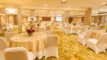 A banquet hall with round tables, white chairs, and floral centerpieces.