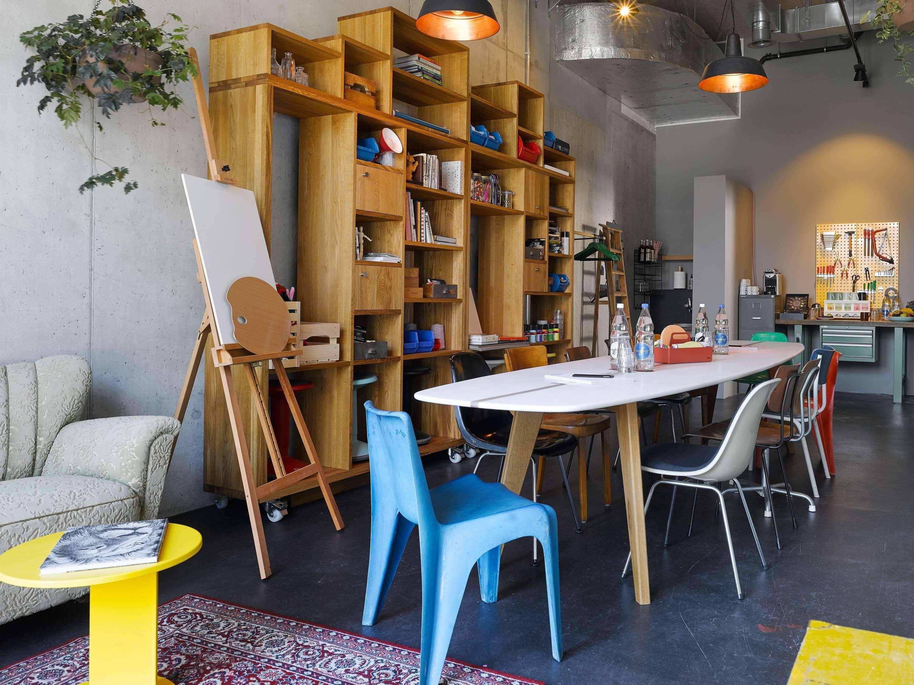 A room with a large wooden bookshelf, a dining table with chairs, a small yellow table, and a blue chair.