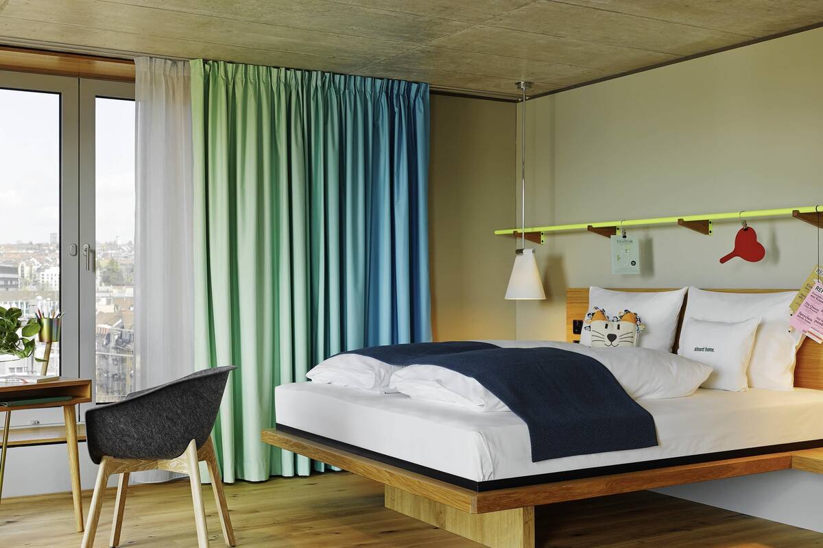 A modern hotel room with a bed, a desk, and a chair.