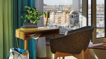 Habitación con escritorio, silla, planta y vista panorámica de un paisaje urbano a través de una ventana.