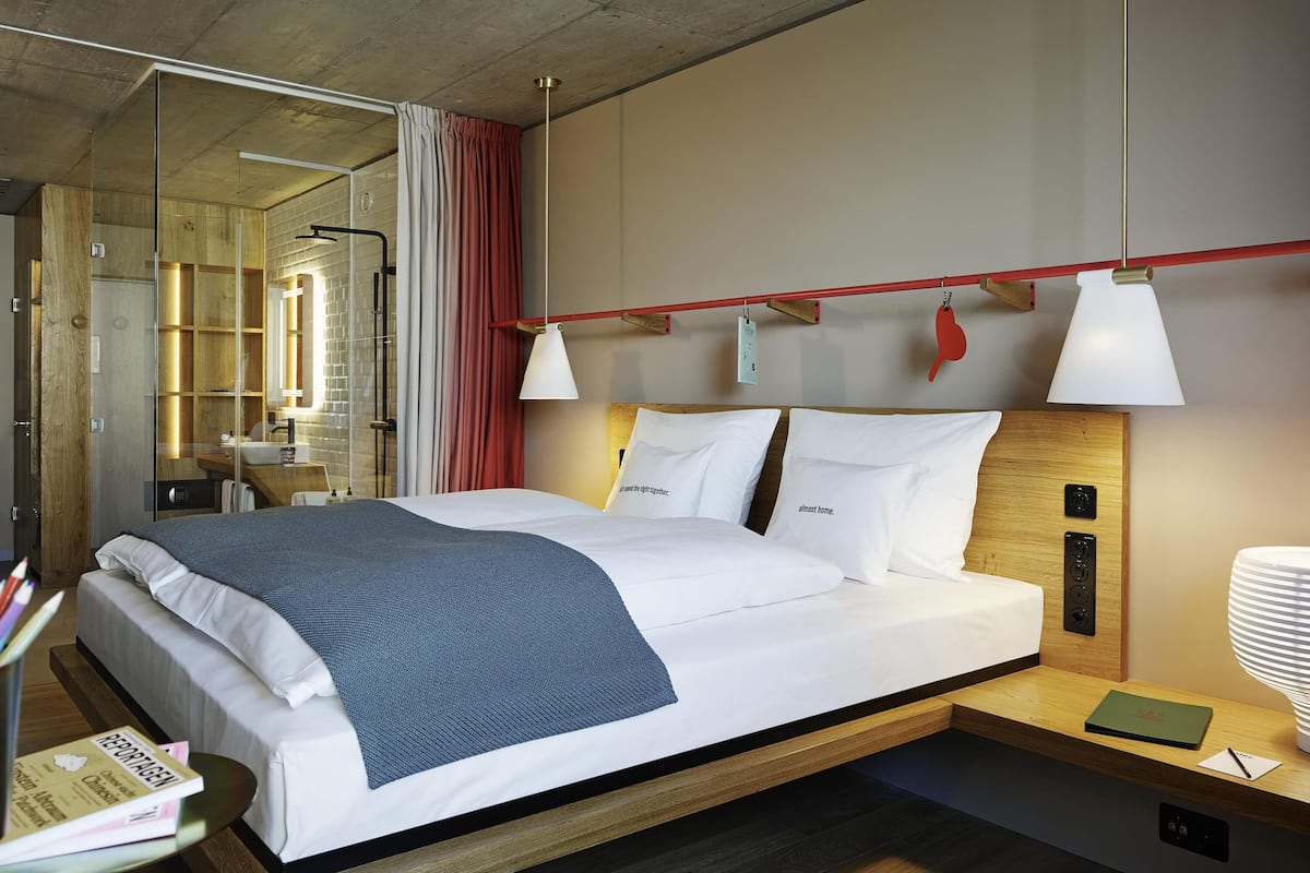 A modern hotel room with a large bed, bedside tables, a desk, and a mirror.