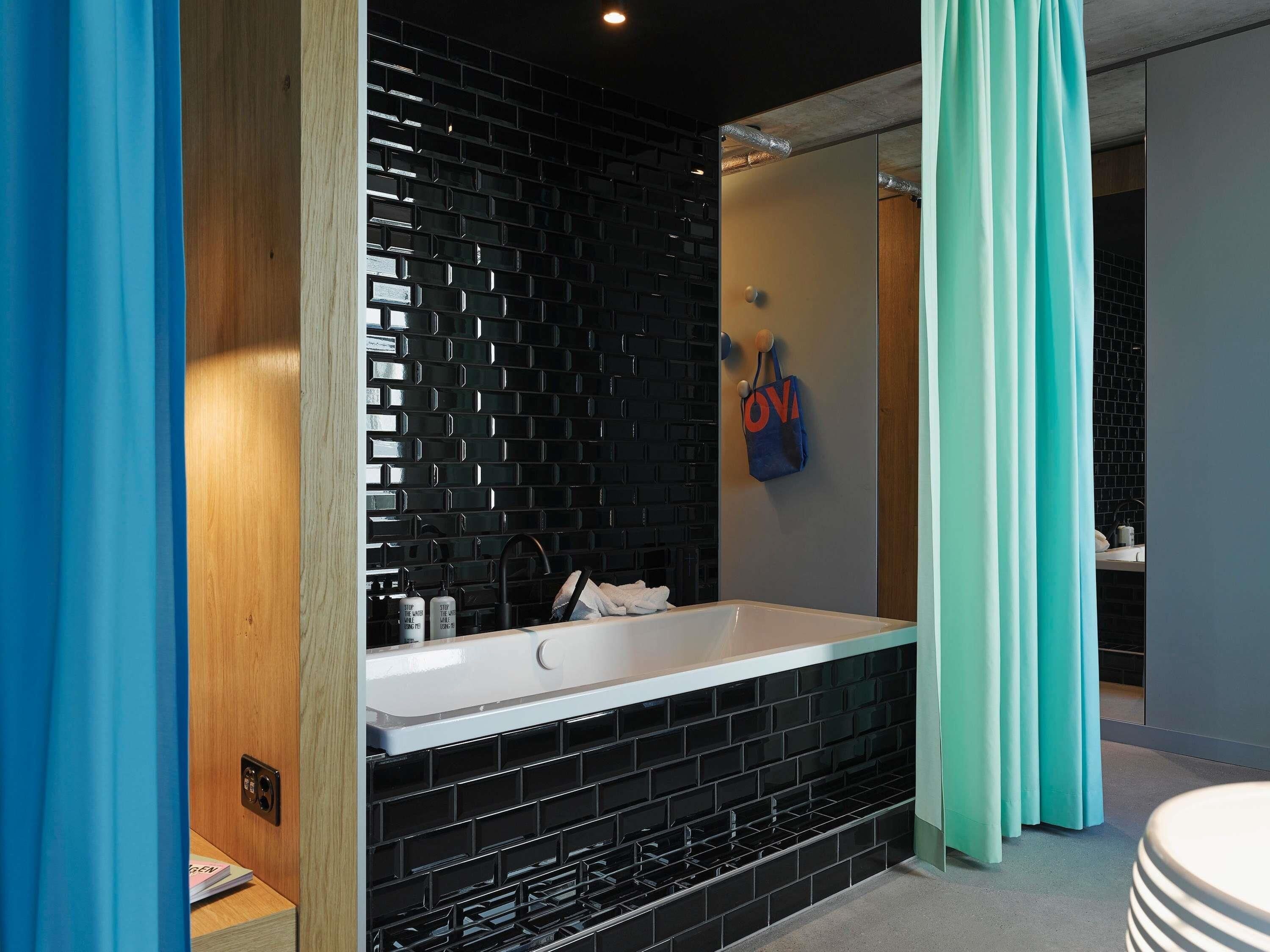 Une salle de bain moderne avec un mur recouvert de carreaux noirs, une baignoire blanche et un rideau bleu.