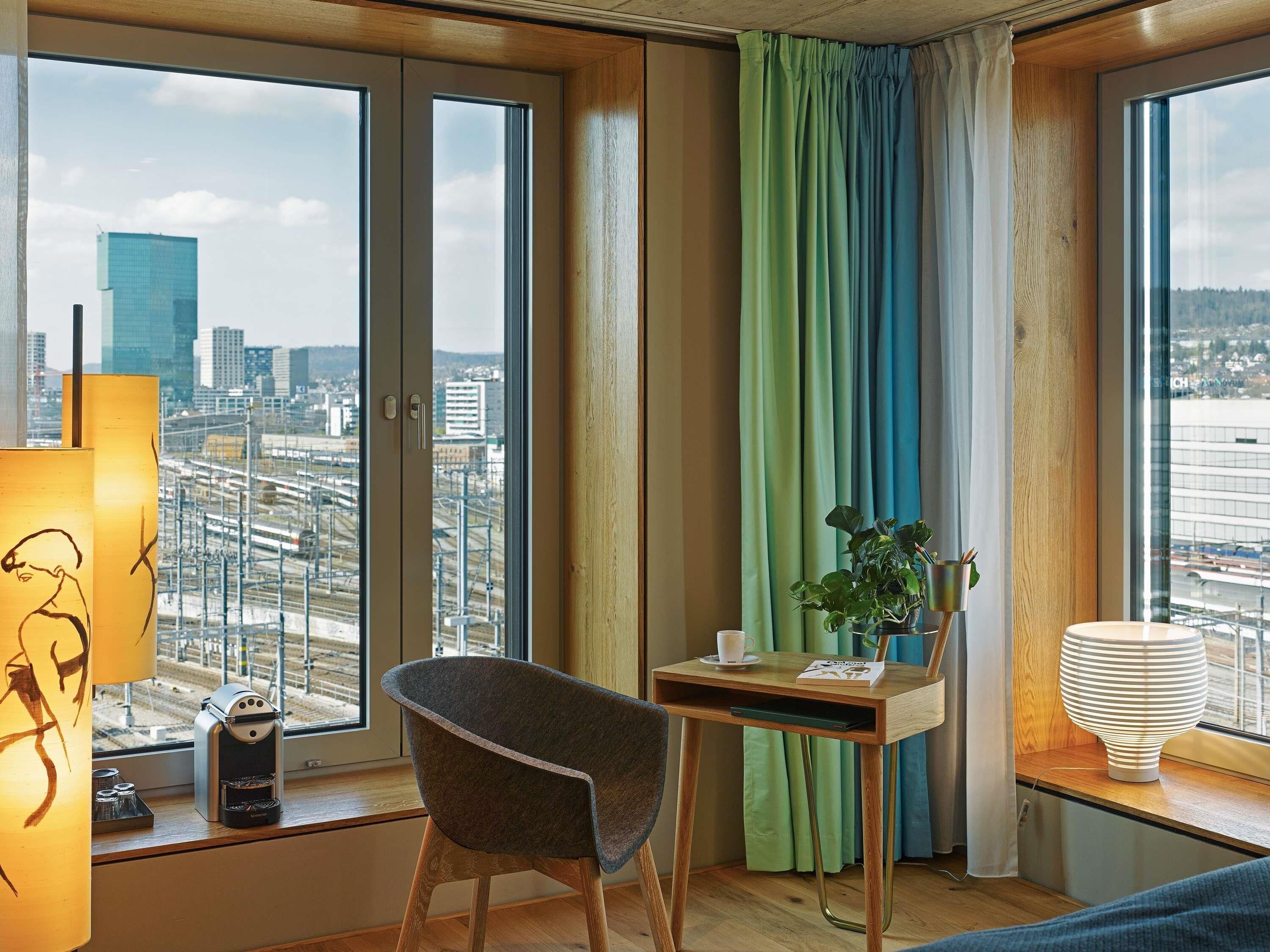 Habitación de hotel con vista a la ciudad, un escritorio con silla, una cafetera y una lámpara.