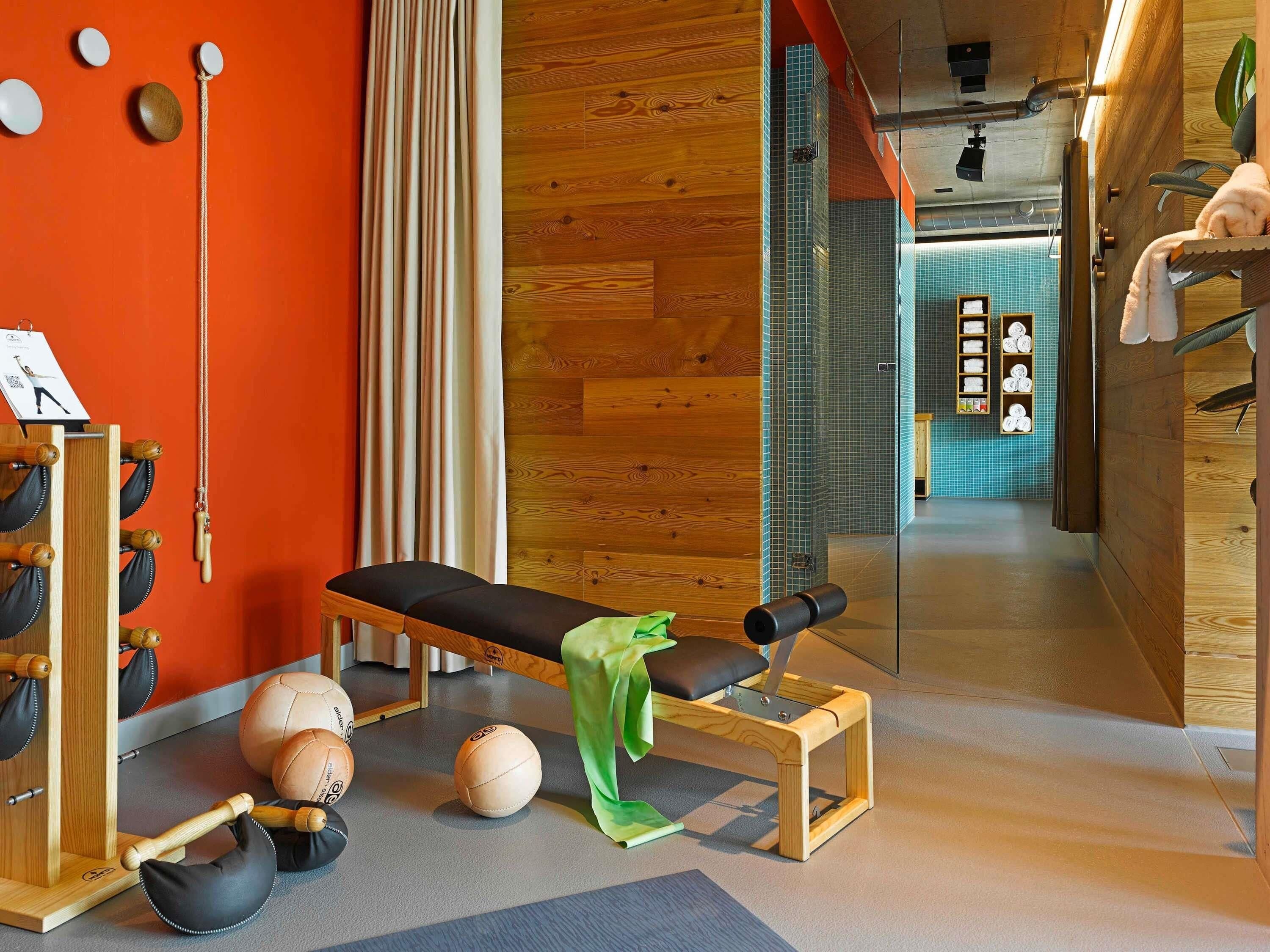 Een kamer met een houten bank, fitnessballen en een wandrek met handdoeken.