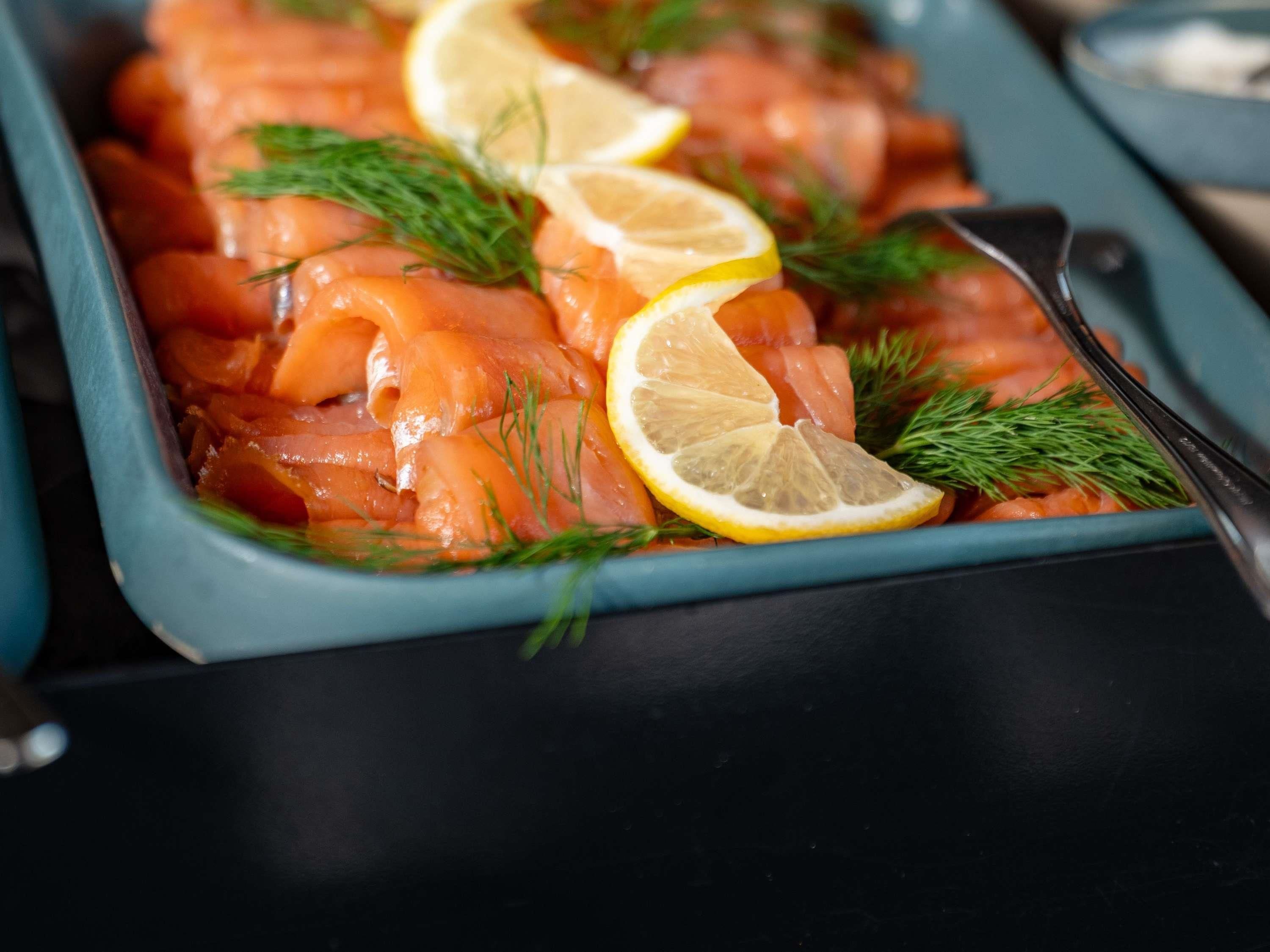 Un plato de salmón ahumado adornado con eneldo y rodajas de limón.