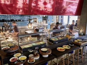 Buffet med forskellige spiser samt et køkken i baggrunden.
