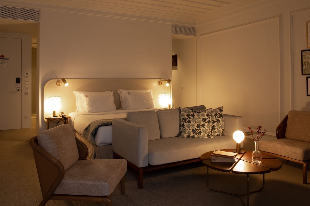 Une chambre d’hôtel comprenant un lit, deux fauteuils, un canapé, une table basse et un mur orné de tableaux.