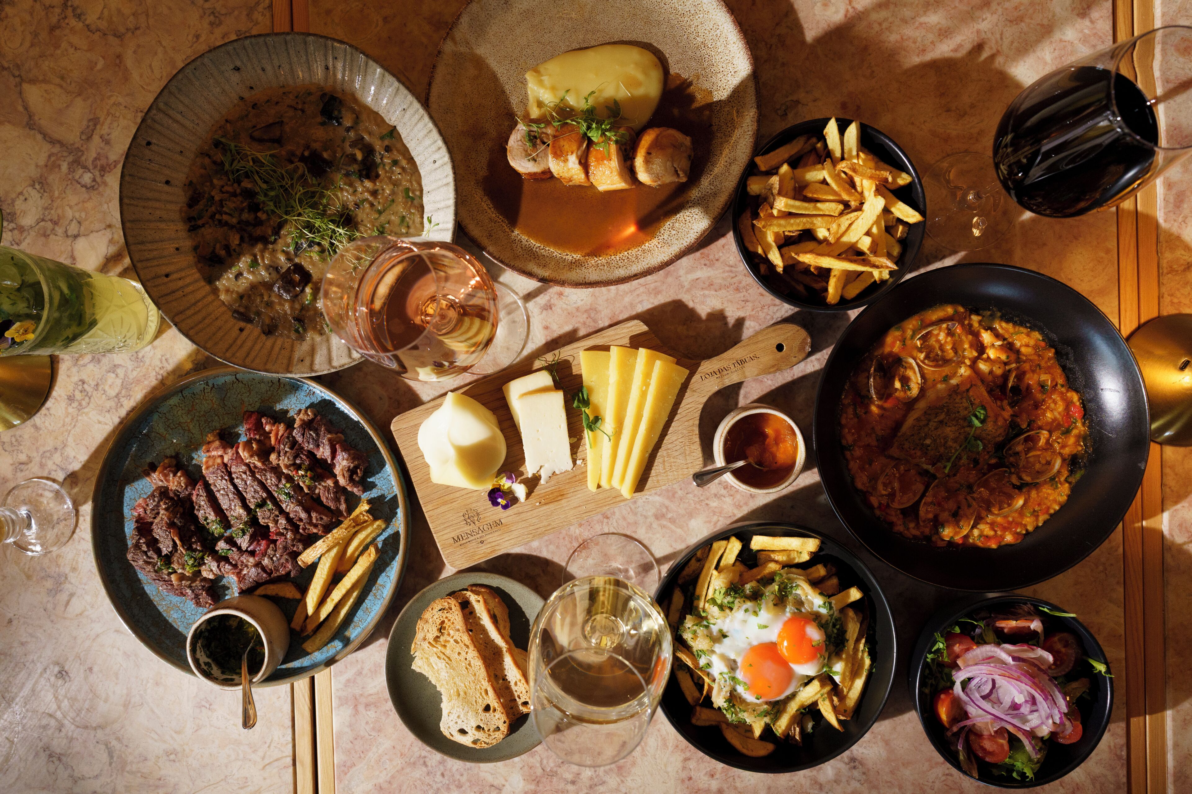 A variety of dishes and drinks on a table, including steak, cheese, and a pan of pasta.